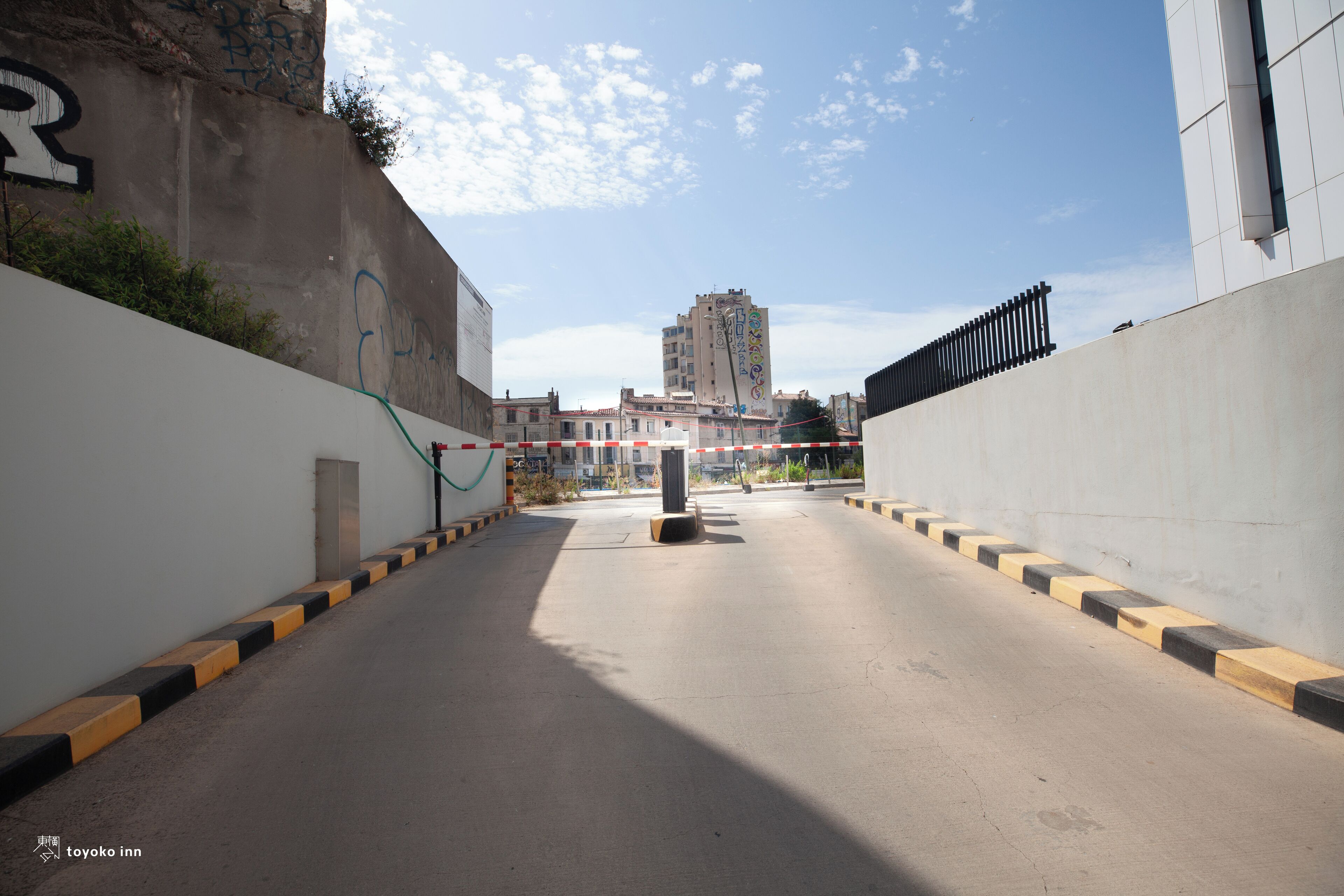 Una calle urbana vacía, con un muro de concreto a la izquierda y un edificio a la derecha.