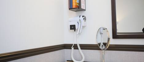 A hairdryer and a mirror on a wall-mounted stand in a hotel room.