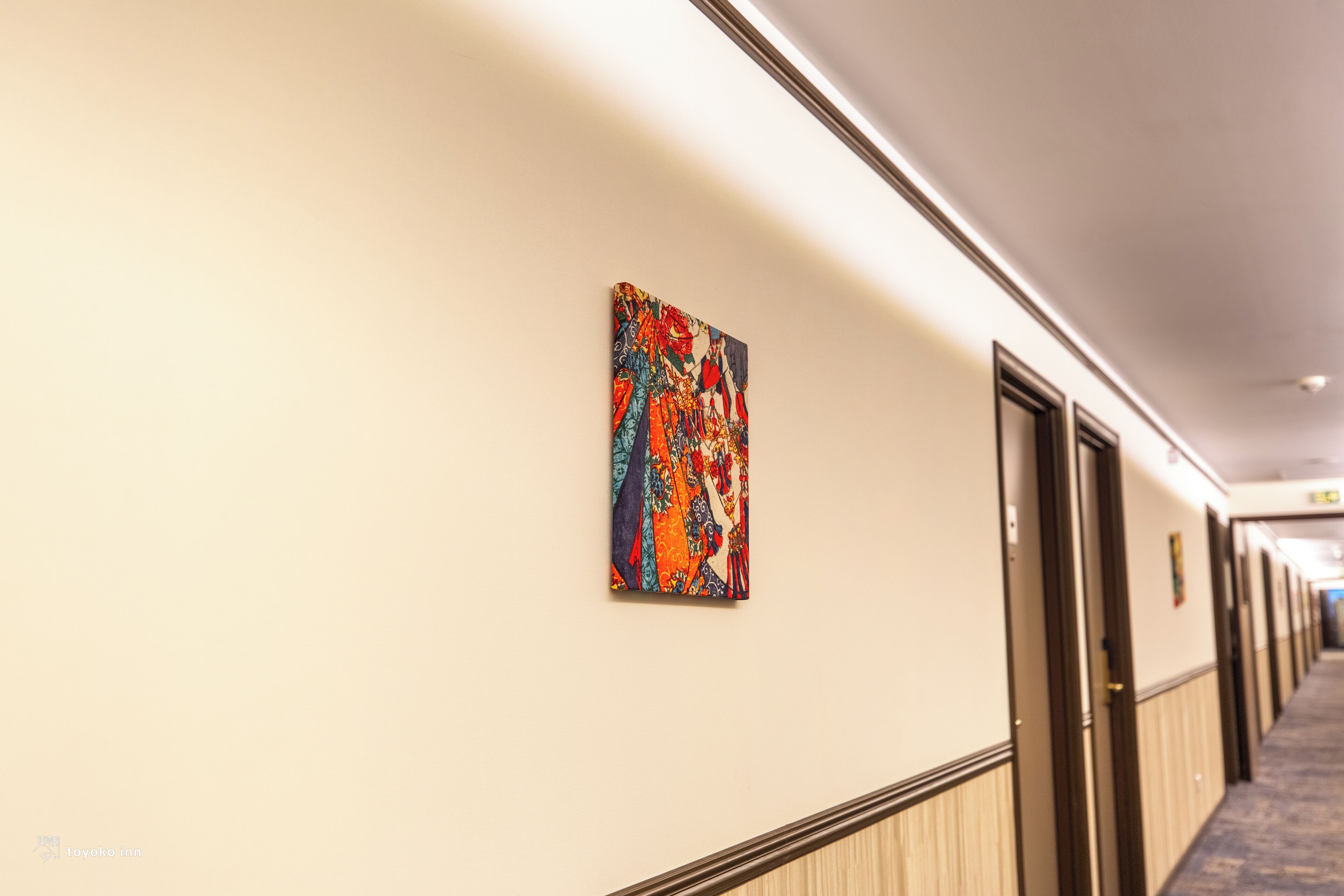 Un couloir d’hôtel orné d’une œuvre d’art colorée sur le mur, les portes et le sol recouvert d’une moquette.