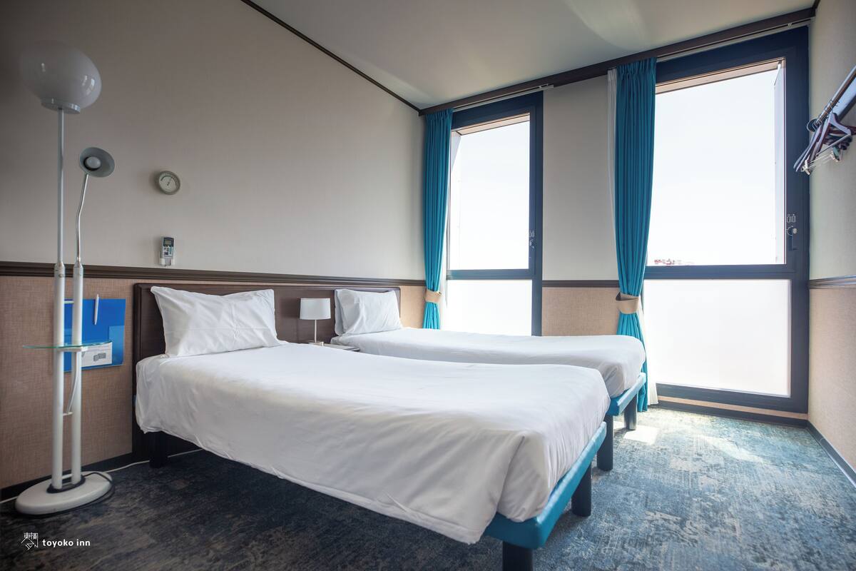 Una camera d'albergo con due letti, una sveglia, una lampada e vista sull'esterno.