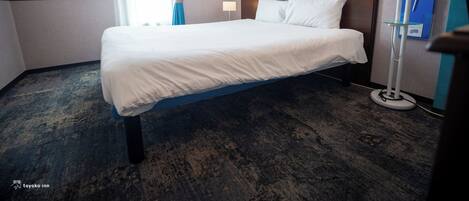 A hotel room with a bed, a bedside table, a lamp, a clock, and a blue curtain.