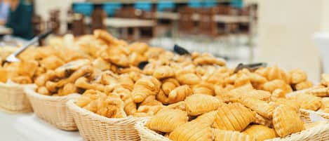 Una mesa de buffet con canastas de cruasanes y otros productos de pastelería.