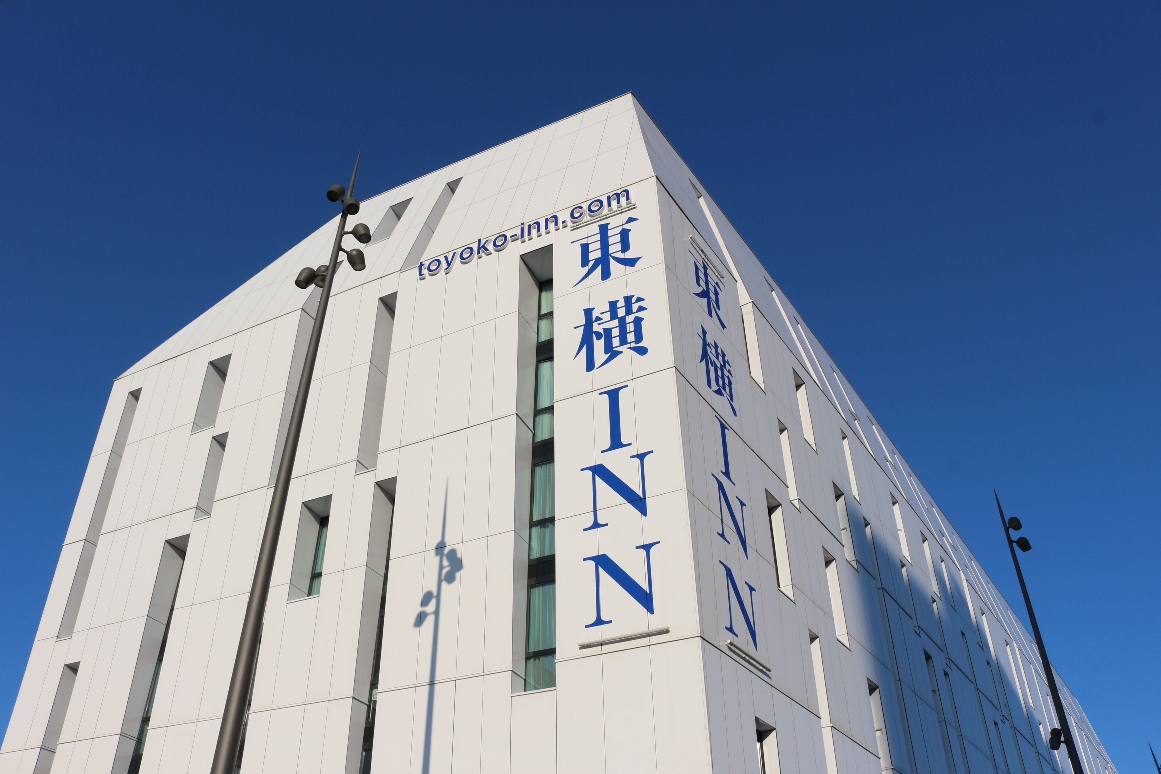 En modern byggnad med skyltar som visar texten ”Toyoko Inn” och ”INN” i stora, blå bokstäver.