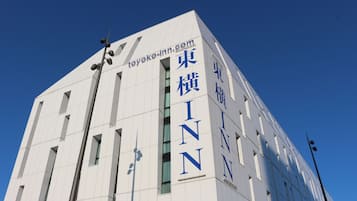 En modern byggnad med skyltar som visar texten ”Toyoko Inn” och ”INN” i stora, blå bokstäver.