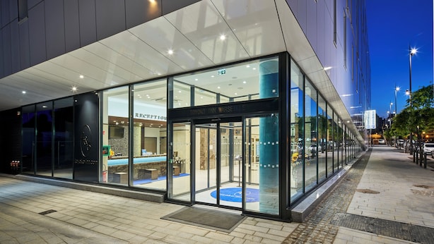 Vestíbulo moderno de hotel con puertas de vidrio, una recepción y alfombra azul.