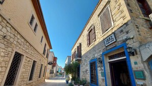 A narrow cobblestone street lined with stone buildings, some with wooden shutters and balconies. - 1882 Butik Otel (Cesme)