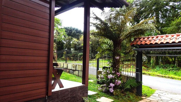 A wooden building with a covered patio area, stone pathway, and a fenced garden with flowering plants. - Chale Bosque da Serra (Canela)