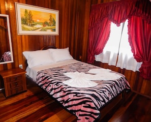 Quarto com painéis de madeira, uma cama, mesa de cabeceira, pintura e cortinas vermelhas.