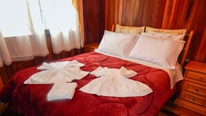 A neatly made bed with a red quilt, white pillows, and folded white towels on the bed. - Chale Bosque da Serra (Canela)