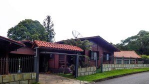 A row of two-story houses with red-tiled roofs, a paved driveway, and a stone wall separating the property from the street. - Chale Bosque da Serra (Canela)