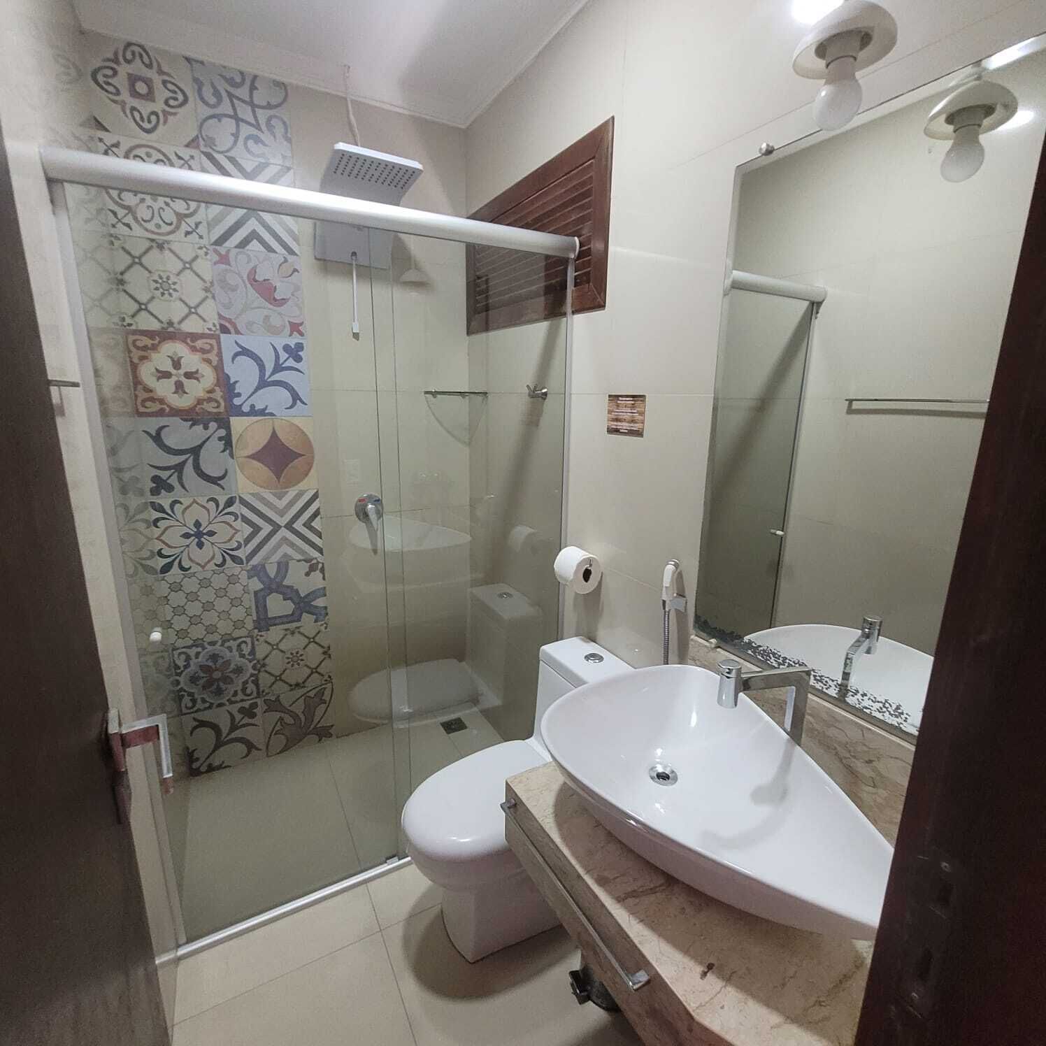 Un baño con ducha de vidrio, inodoro y lavamanos con espejo.