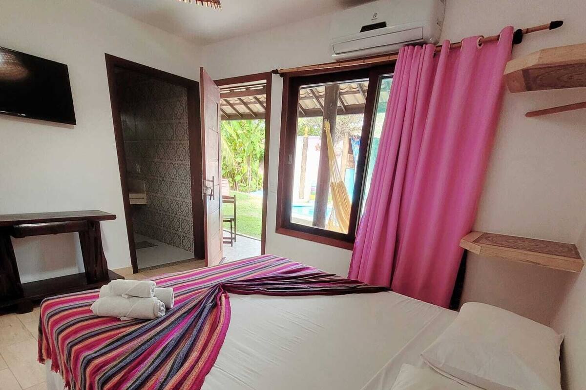 A bedroom with a bed, a TV, a desk, and a view of the outdoors.