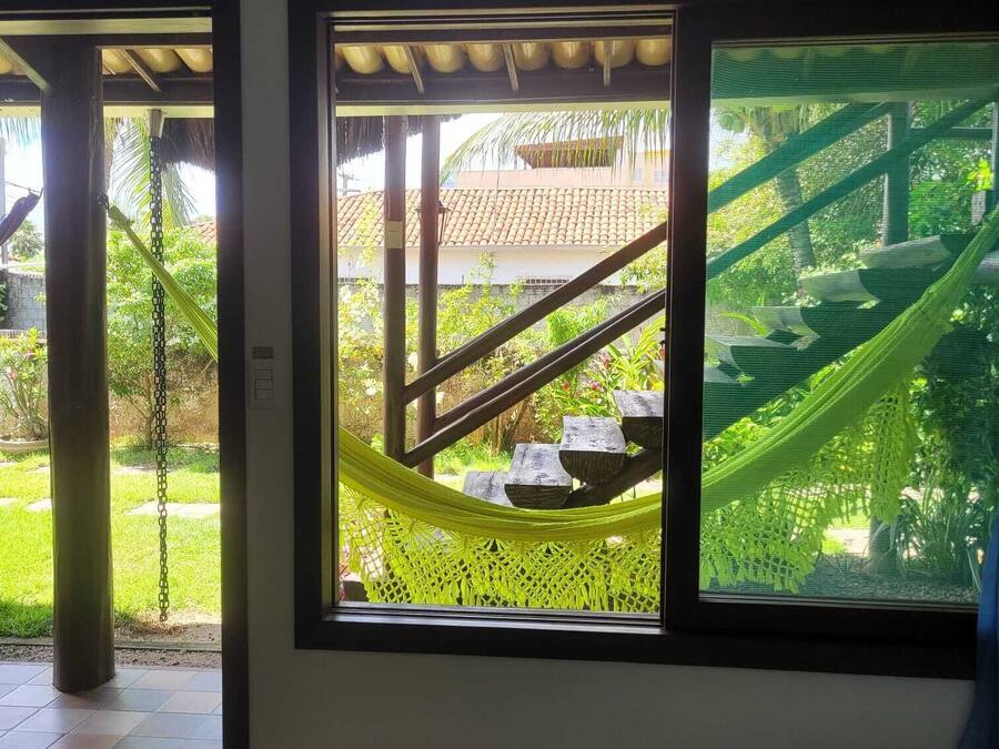 A room with a large window overlooking a garden with a hammock and a staircase.
