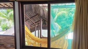 Una habitación con un ventanal grande que da a una hamaca y una estructura de techo de paja, con un equipo de aire acondicionado arriba.