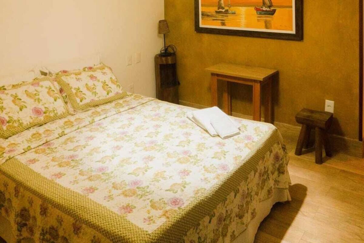 A bedroom with a bed, a nightstand, a small table, and a painting on the wall.