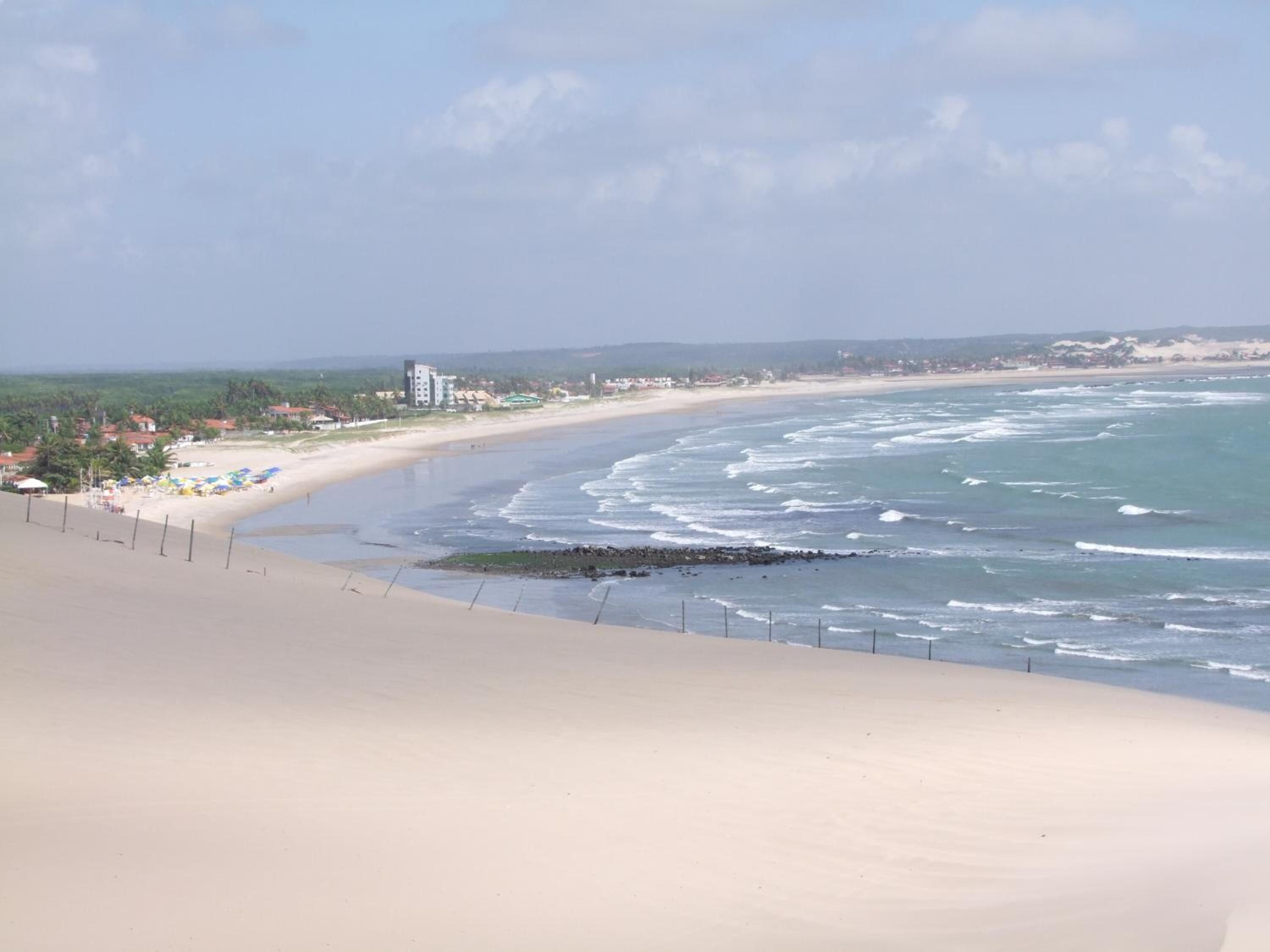 Una playa con arena, algunas sombrillas y edificios a lo lejos.