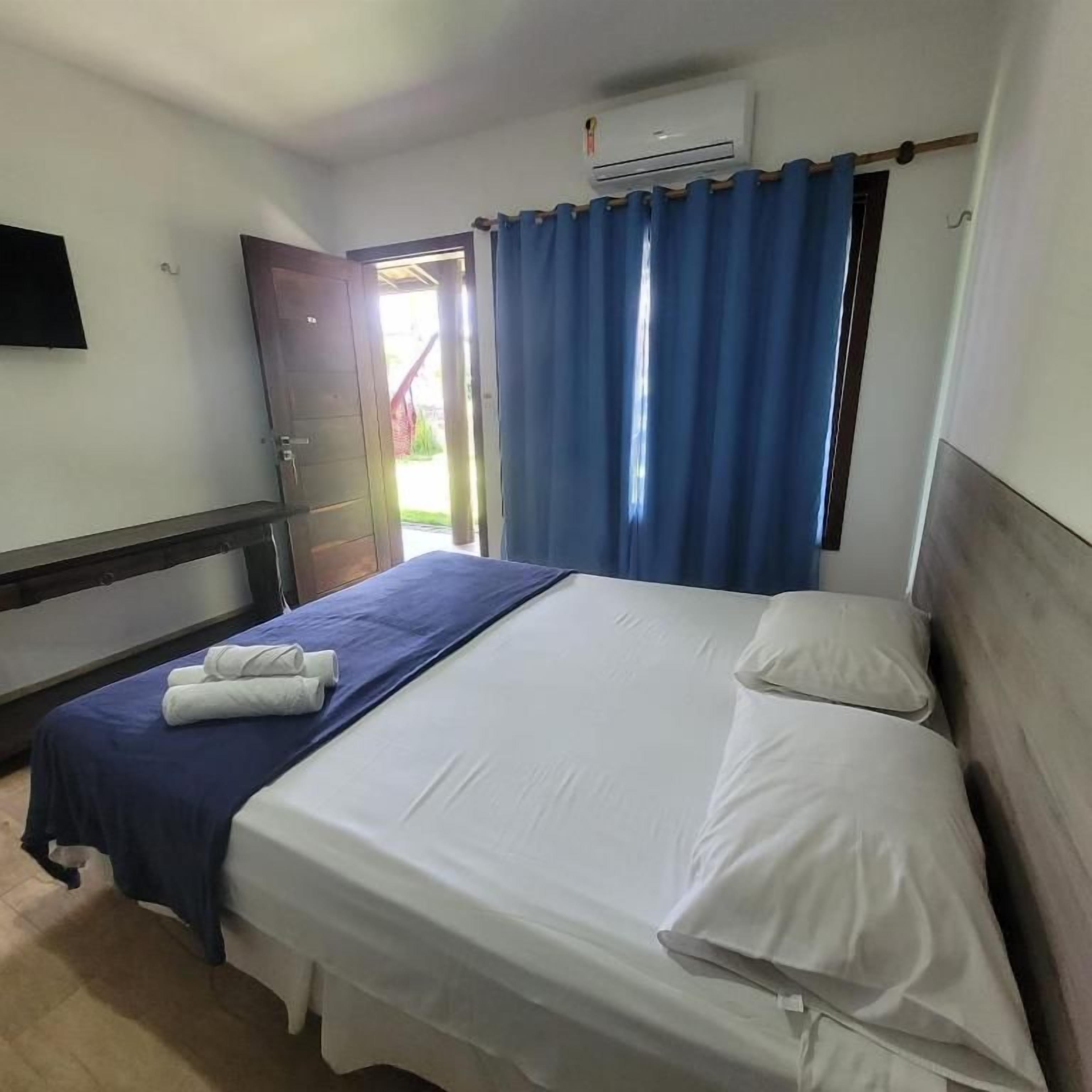 A hotel room with a bed, a blue curtain, a white wall, and an air conditioning unit.