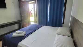 A hotel room with a bed, a blue curtain, a white wall, and an air conditioning unit.