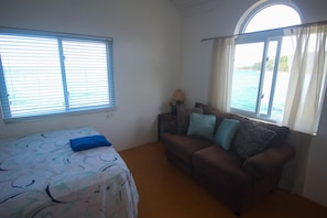 Una habitación con cama, un sofá marrón y ventana con vistas al mar.