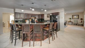 A spacious kitchen with a central island, dark wooden bar stools, and pendant lighting.