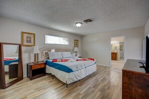A bedroom with a bed, a nightstand, a mirror, a window, and a door leading to a bathroom.