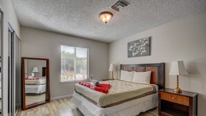 A bedroom with a large bed, two bedside tables, a mirror, and a window with blinds.