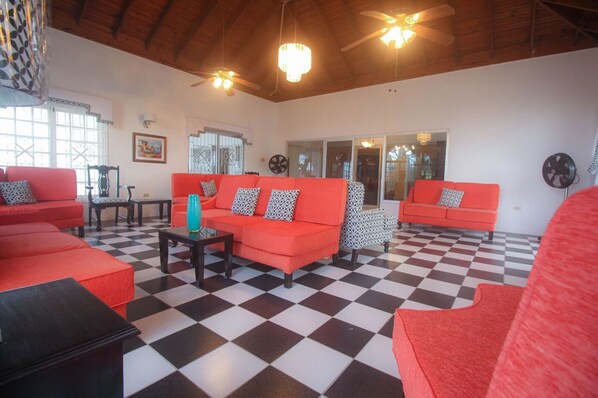 A spacious living area with red sofas, a checkered floor, and ceiling fans.