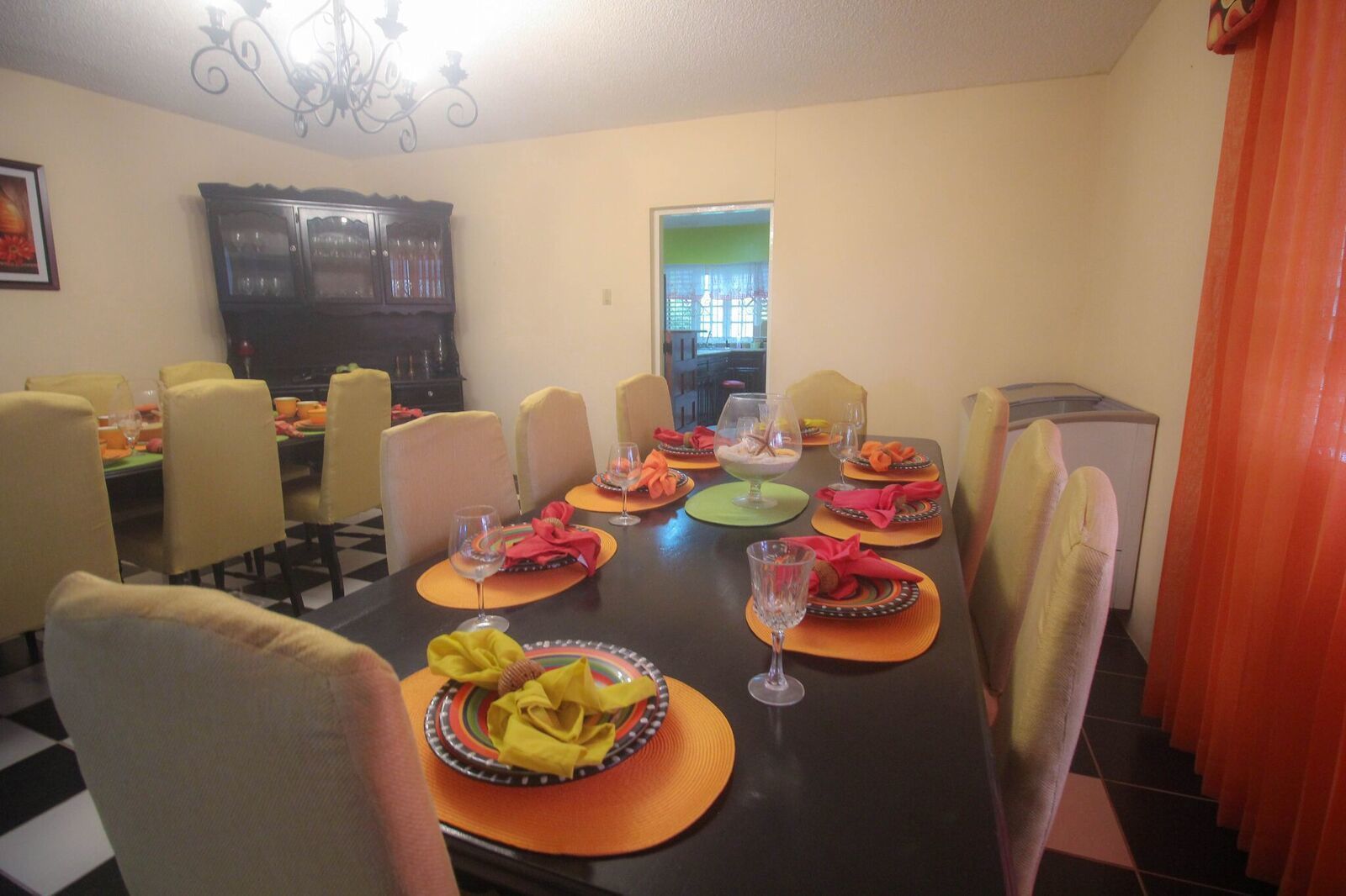 Ein Esszimmer mit einem langen Tisch, der für eine Mahlzeit gedeckt ist, Stühle darum herum und einem Fernseher im Hintergrund.
