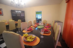 A dining room with a long table set for a meal, chairs around it, and a television in the background.