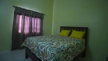 A bedroom with a bed, curtains, and a yellow pillow.