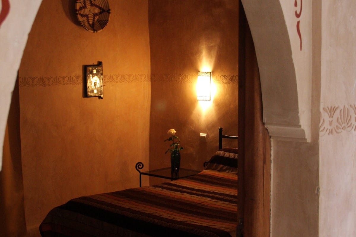 A bedroom with a bed, a wall-mounted clock, and a wall-mounted light fixture.