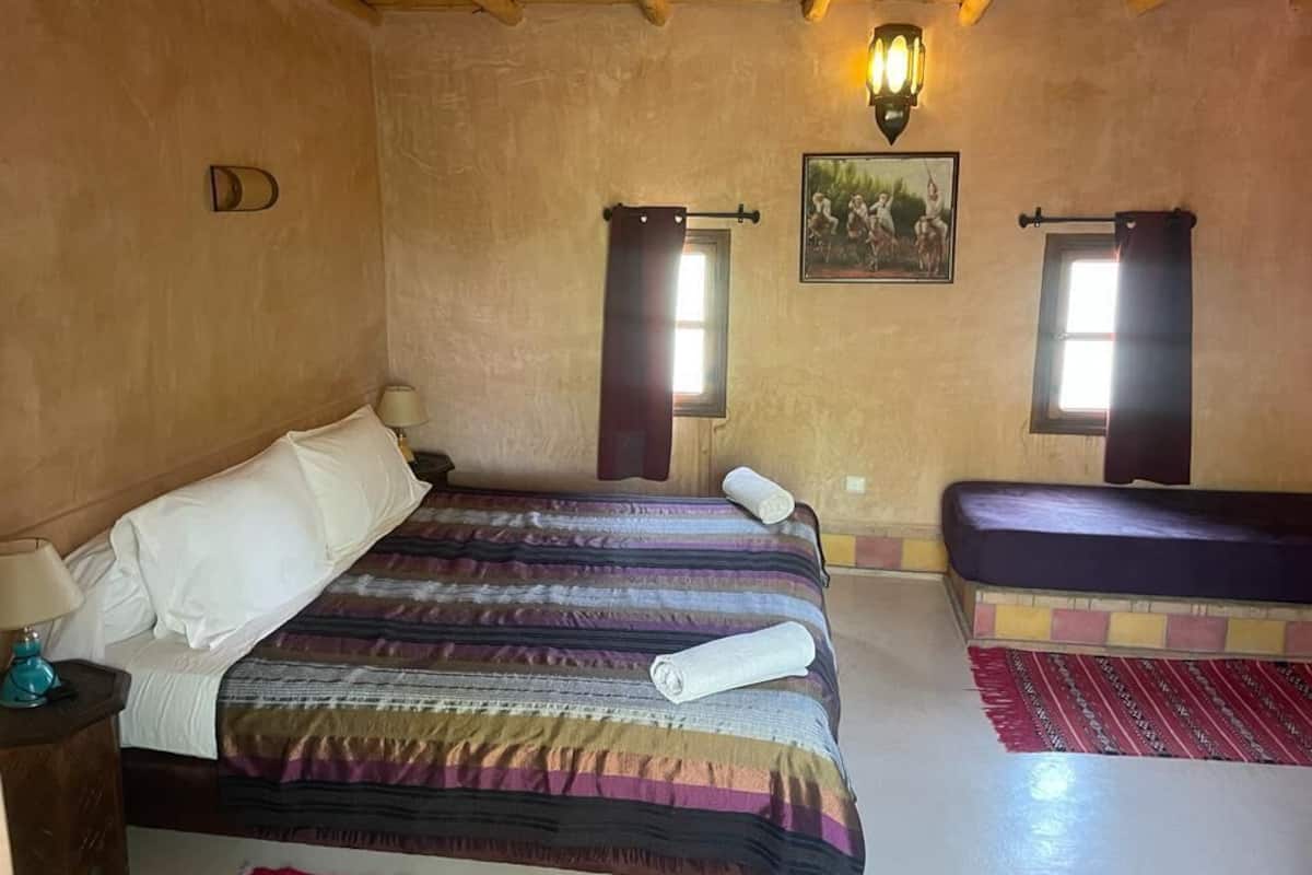 A bedroom with a bed, a bench, a wall-mounted light, and a window.