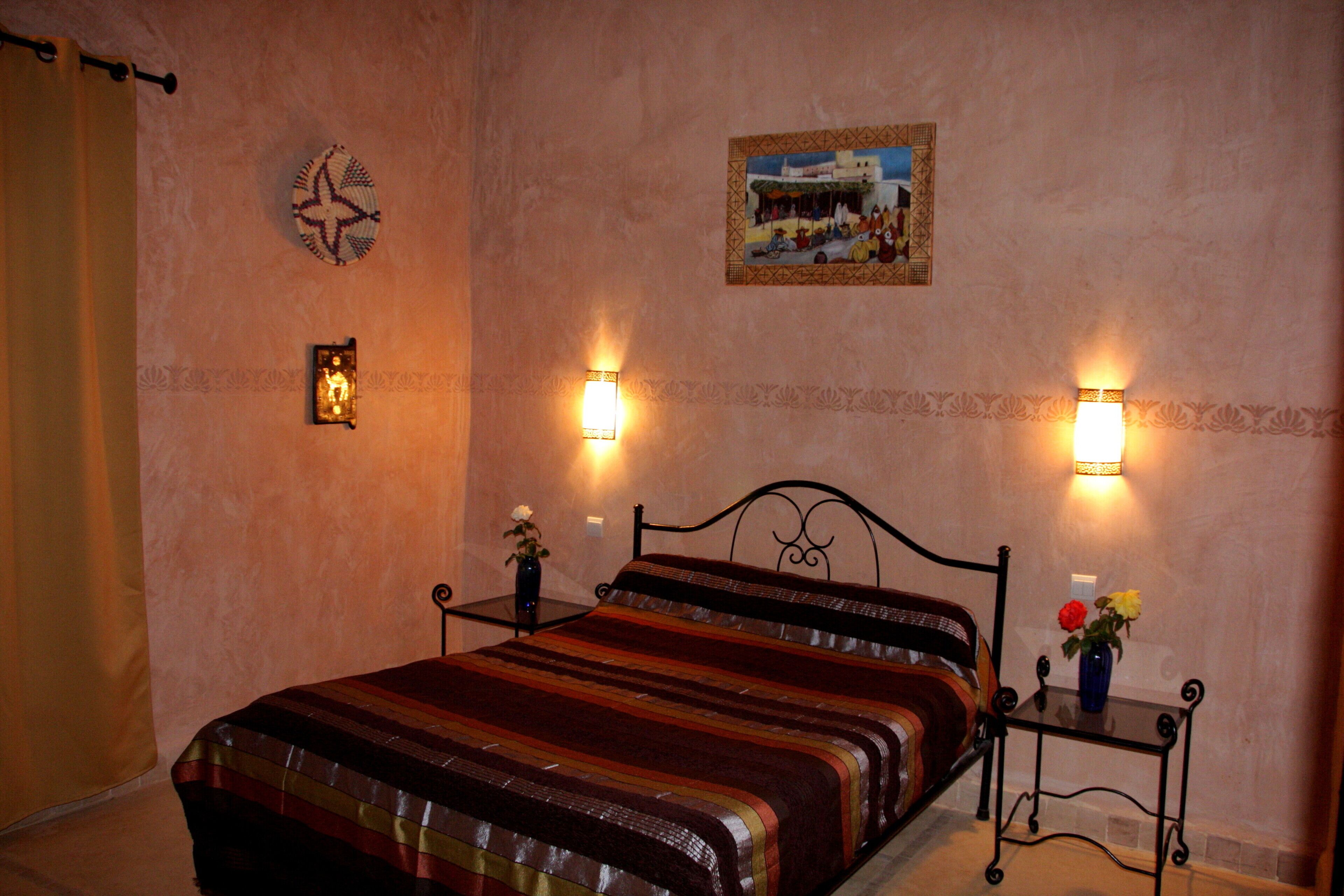 A bedroom with a bed, two wall-mounted lamps, a small table with a vase, and a wall decoration.