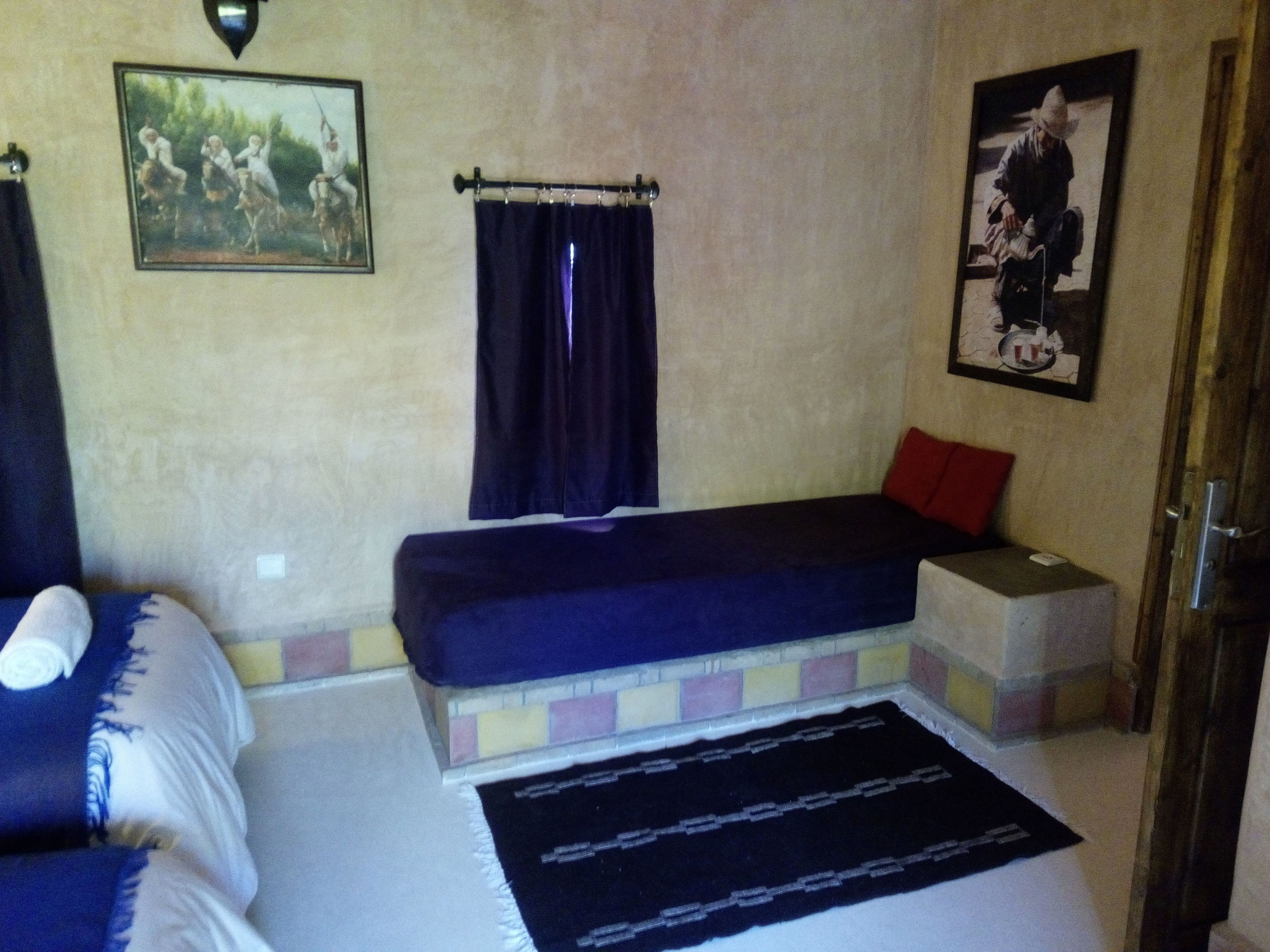 A room with a bed, a bench, a rug, and two paintings on the wall.