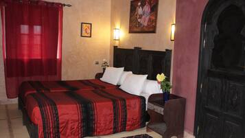 A hotel room with a large bed, a nightstand with a vase of flowers, a wall-mounted painting, and a dark wooden door.