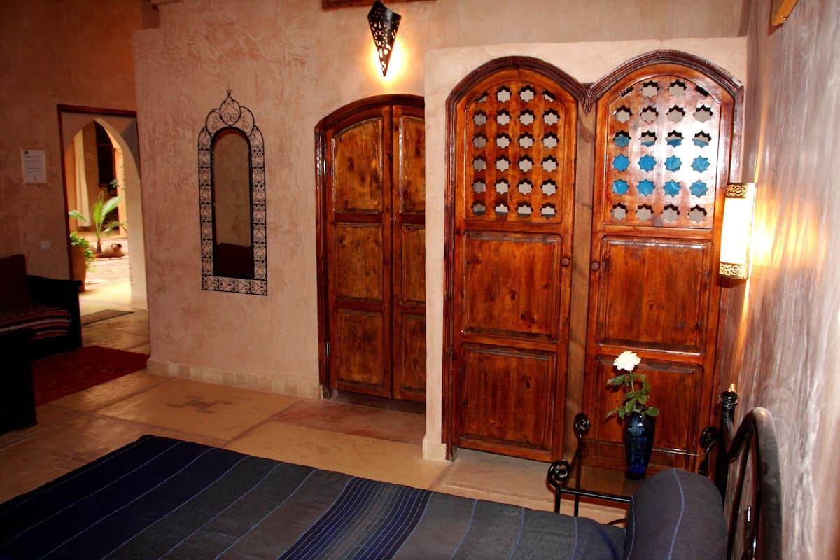A room with a large wooden door, a mirror, and a small table with a vase of flowers.