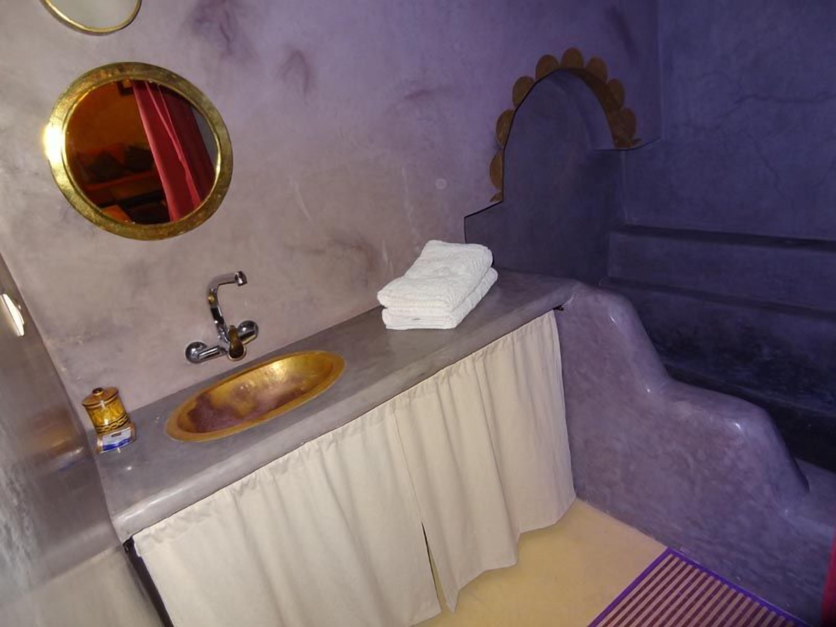 A bathroom with a gold sink, a mirror, and a towel rack.