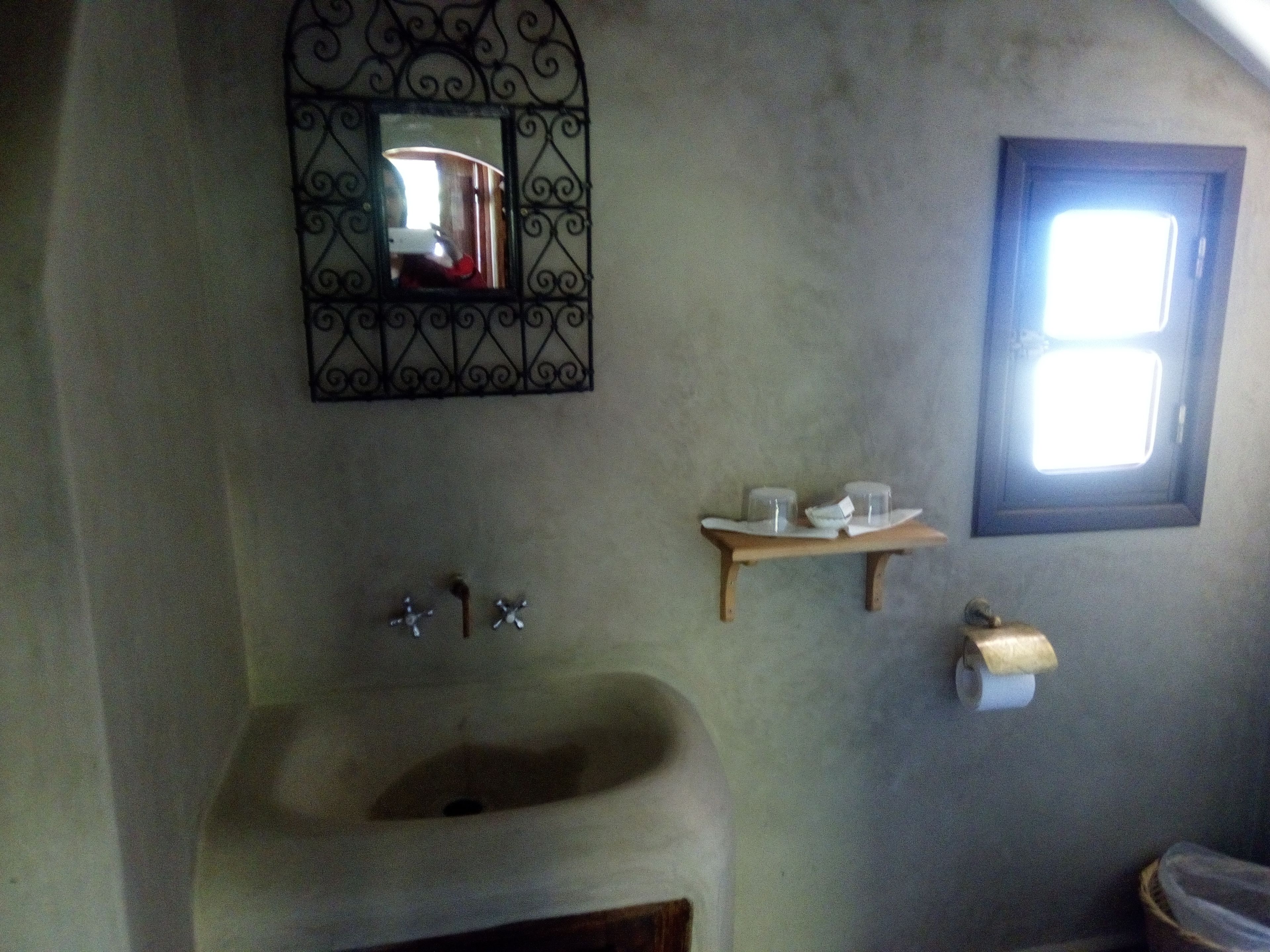 A bathroom with a sink, mirror, shelf with toiletries, and a window.
