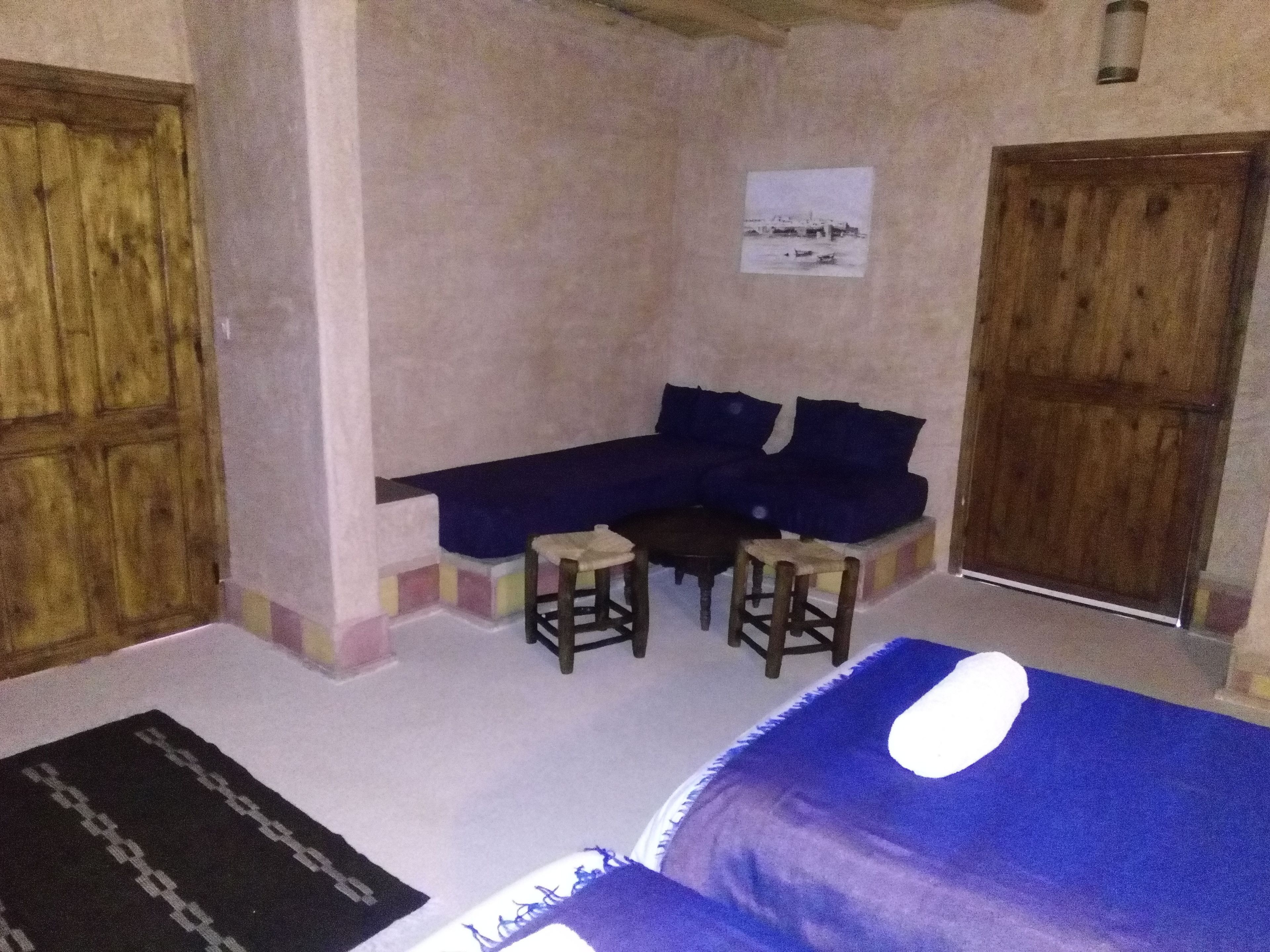 A room with a blue sofa, two stools, a small table, and a wooden door.