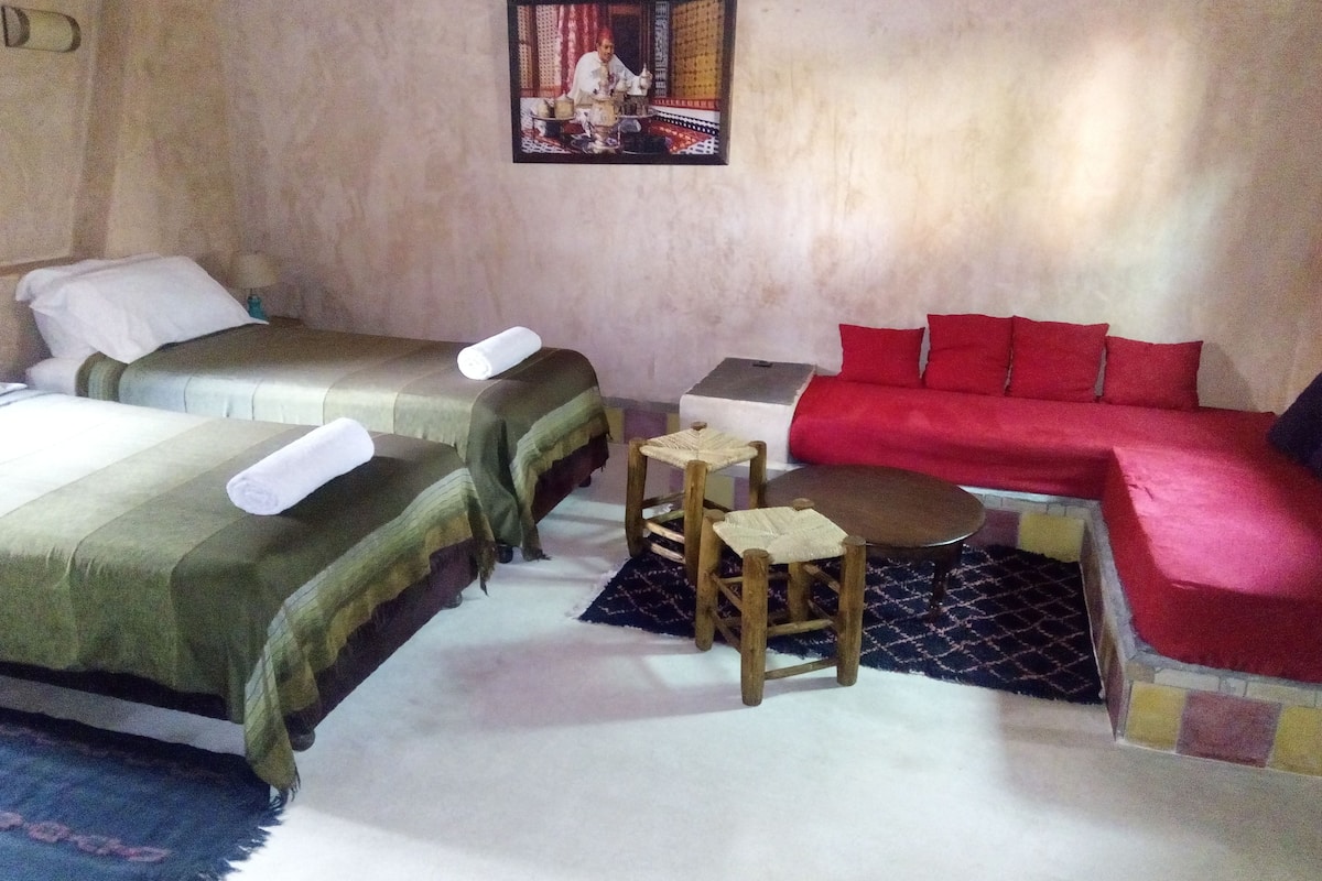A room with two single beds, a small table, a red sofa, and a wall-mounted picture.