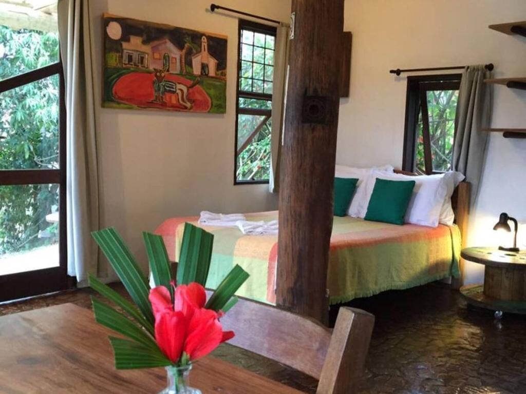 Una habitación con una cama, una silla de madera, una mesa con una lámpara y un cuadro en la pared.