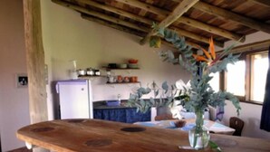 A rustic kitchen with a wooden bar counter, a refrigerator, and various kitchen items on shelves. - Pousada Gopak (Imbituba)