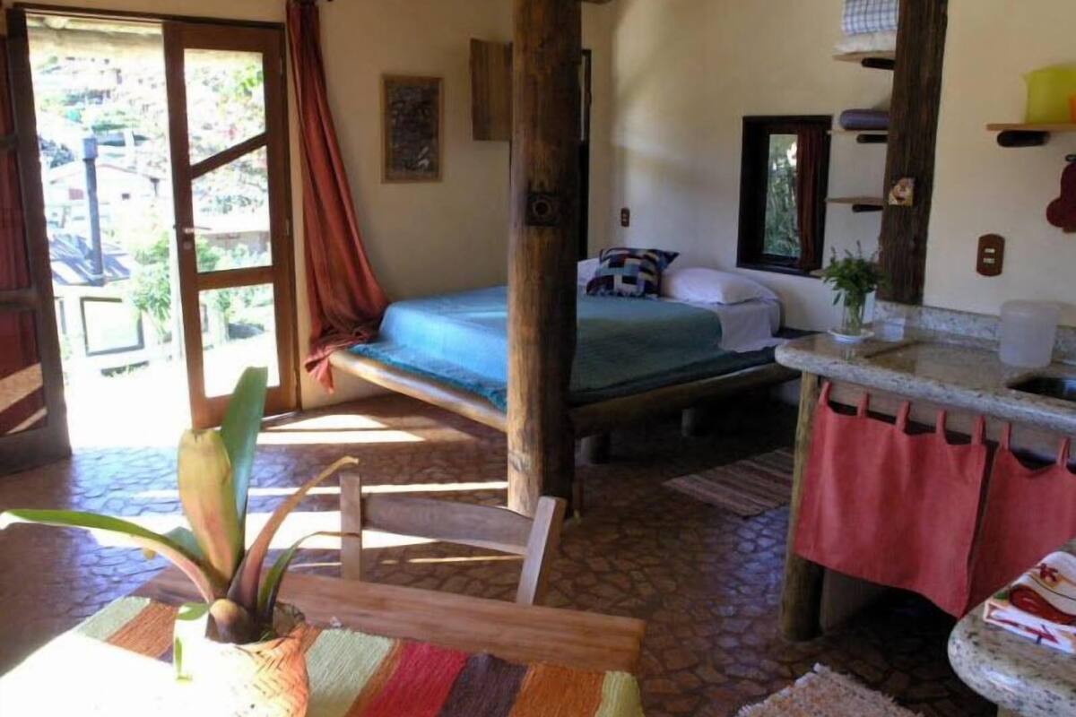 A room with a bed, a small table, a chair, a sink, and a window with curtains.