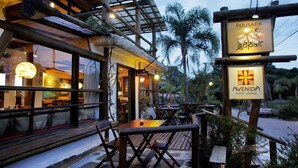 An outdoor dining area with wooden tables and chairs, a sign for 'Pousada Gopark', and another sign for 'Avenida Pizza Lounge'. - Pousada Gopak (Imbituba)