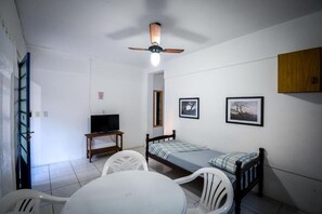 A small, clean room with a bed, a desk with a television, a ceiling fan, and a dining area with chairs and a table. - Pousada Natureza (Florianópolis)