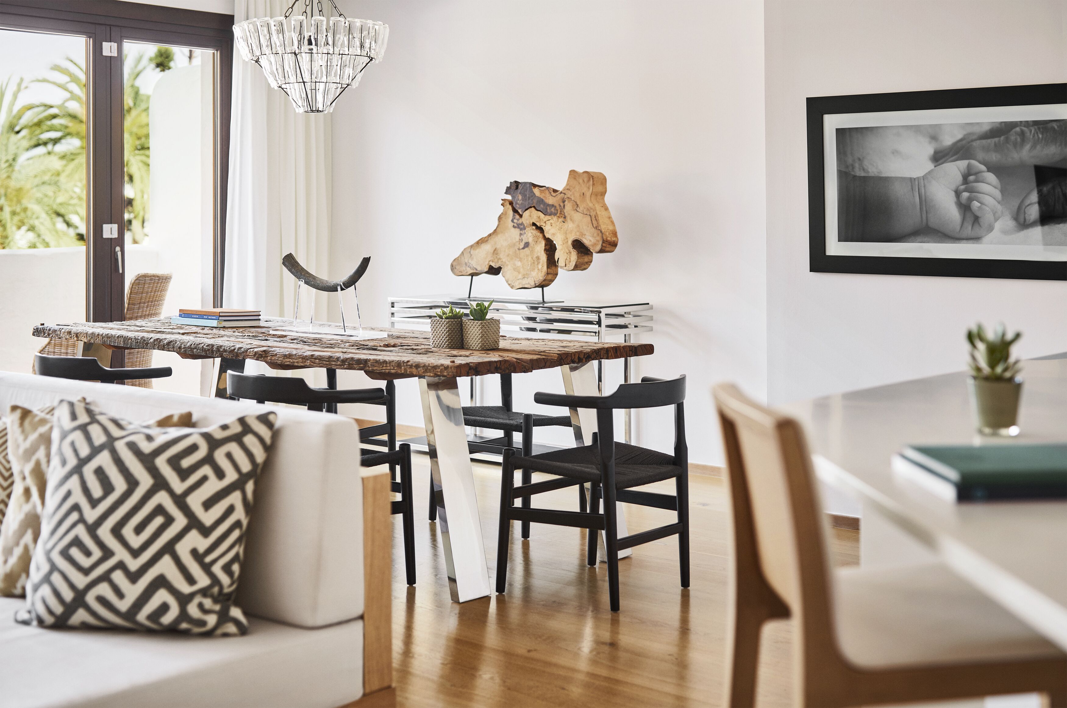 Ein modernes Wohnzimmer mit einem Holzes Esstisch, schwarzen Stühlen, einem weißen Sofa und einer Kronleuchter.