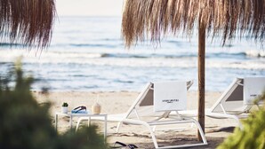 A beach scene with two white lounge chairs labeled "NOBU HOTEL" and a small table with a plant and a bottle. - Nobu Hotel Marbella (Marbella)