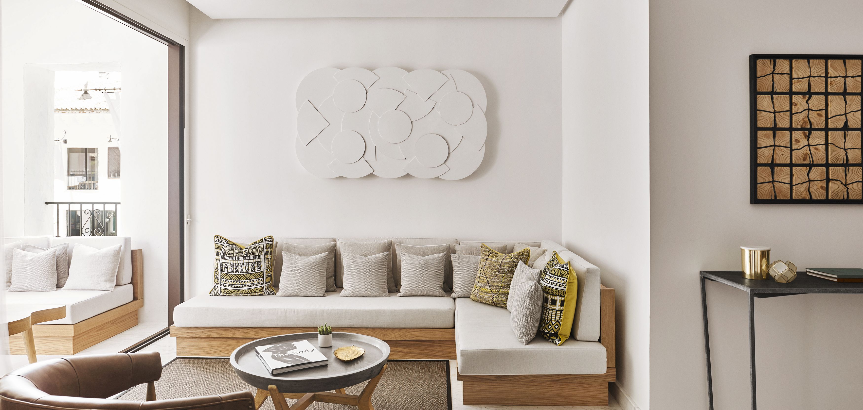 A modern living room with a white sofa, patterned cushions, a round coffee table, and a wall art piece.