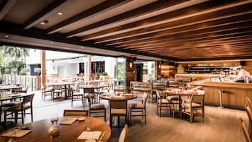 Een ruim restaurant met houten balken, meerdere eettafels en een bar.