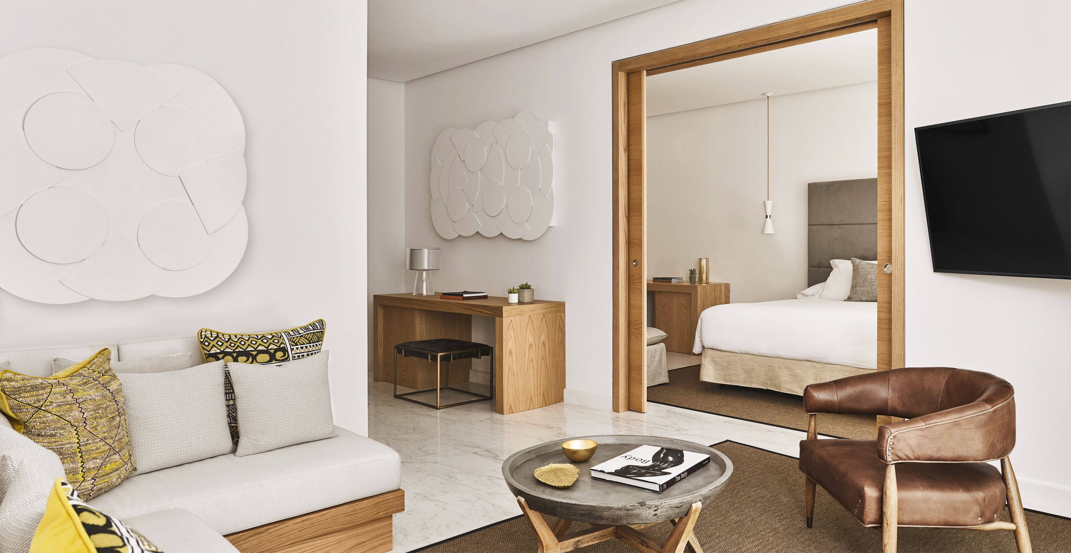 A modern hotel room with a sofa, a desk, a chair, a bed, and a TV.